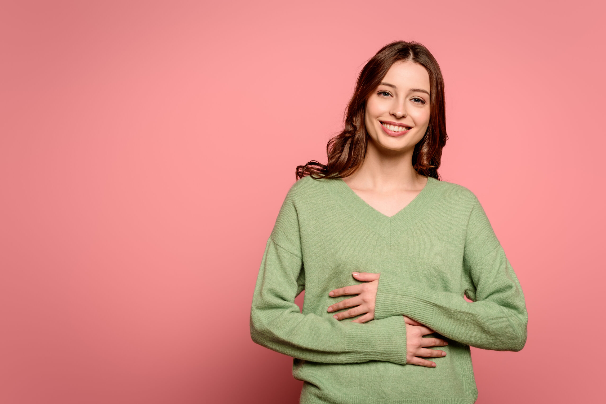 excited girl laughing while holding hands on stomach on pink background