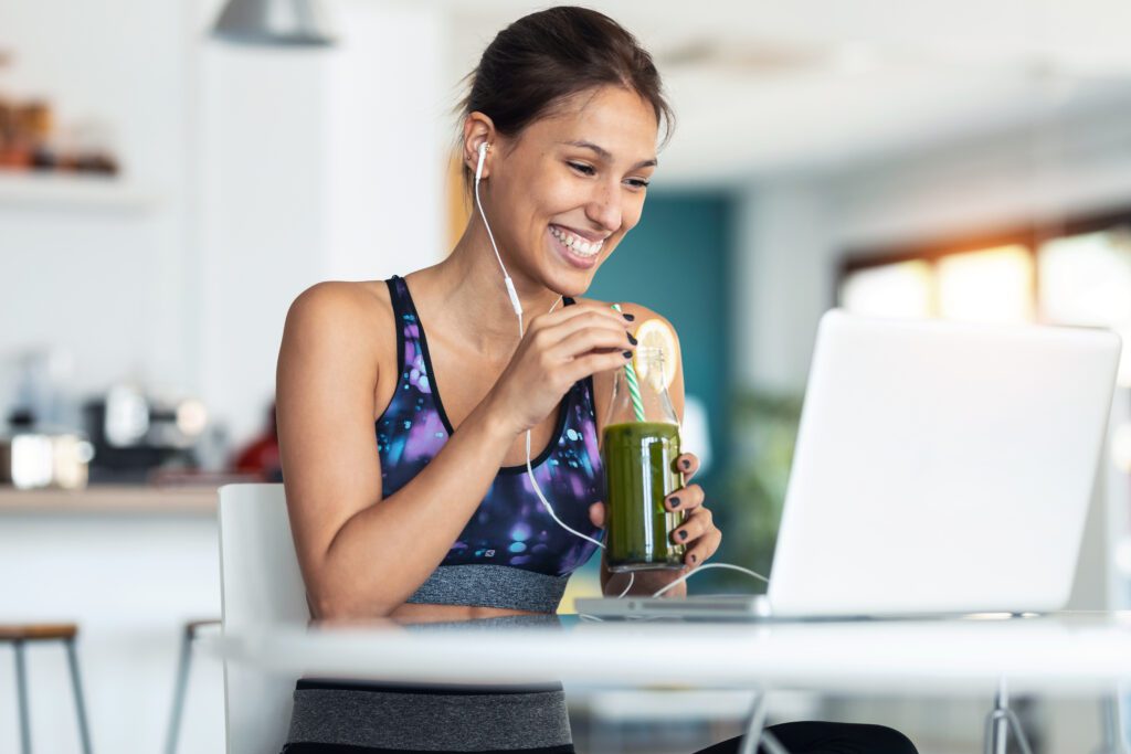 Mulher em frente ao computador, sorrindo e tomando chá verde.