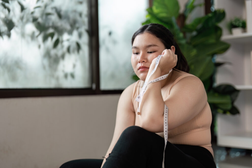 Mulher contemplativa com sobrepeso com fita métrica em ambiente doméstico